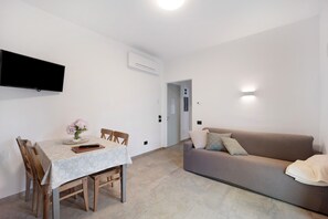 A modern living room with a dining table, sofa, flat-screen TV, and air conditioning unit.