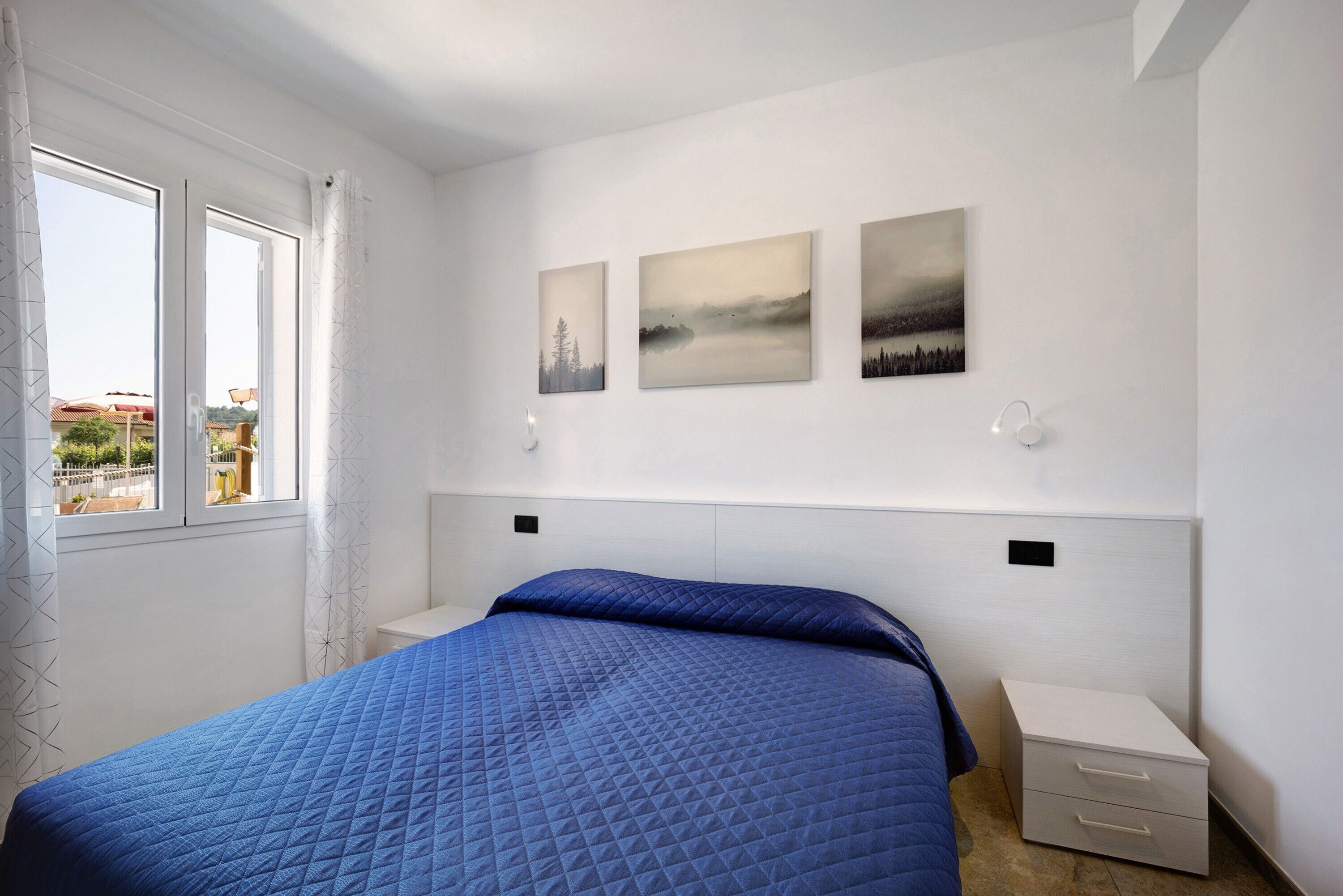 Un dormitorio con una cama, una mesita de noche y tres cuadros colgados en la pared.