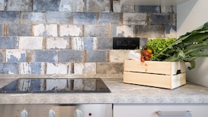 Una cocina con salpicadero de piedra, un cesto de madera con verduras y una estufa moderna.