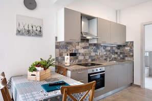 A modern kitchen with a built-in stove, oven, and sink. There is a dining table with chairs and a decorative plant on it. - Holiday Apartment "Antichi Ricordi - Le Giare" with 2 Balconies, Shared Pool & Wi-Fi (Andora)