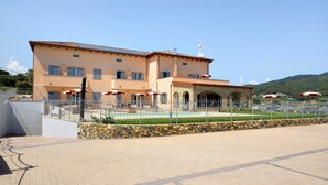 A multi-story building with a tiled roof, a stone wall, and a fenced courtyard with umbrellas. - Holiday Apartment "Antichi Ricordi - Il Fienile" with Balcony, Shared Pool & Wi-Fi (Andora)