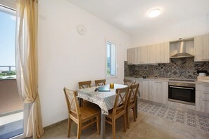 A dining table with chairs, a clock, a window, and a kitchen with cabinets and an oven.