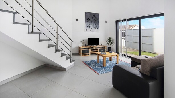 Una sala de estar moderna con una escalera, un televisor de pantalla plana, un mueble de entretenimiento de madera, un sofá y un ventanal grande.