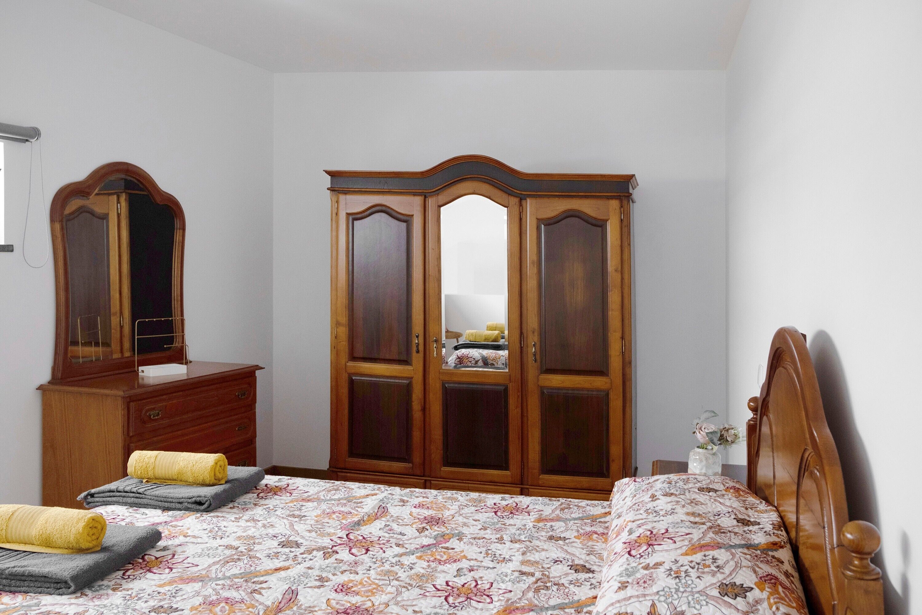 Une chambre à coucher comprenant un lit, une armoire, une commode et un miroir.