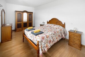 A bedroom with a wooden bed, a wardrobe, a nightstand, and a dresser.