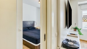 Un dormitori modern amb llit, taula de nit, làmpada i televisió penjada a la paret.