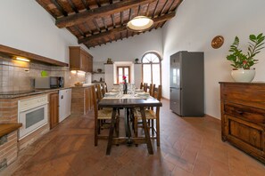 A kitchen with a dining table, wooden cabinets, a refrigerator, and a potted plant. - Agriturismo 'Villa Adelmo' with Private Pool, Terrace, and Wi-Fi (Pomarance)