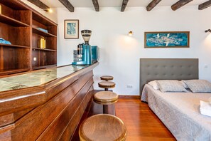 Une chambre à coucher comprenant un lit, une tête de lit, une machine à café, une étagère avec divers objets et un tableau accroché au mur.