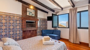 Un dormitorio con chimenea, sofá azul y ventana grande con cortinas.