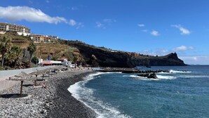 Una playa costera con costa rocosa, cielo azul claro y edificios en una colina.