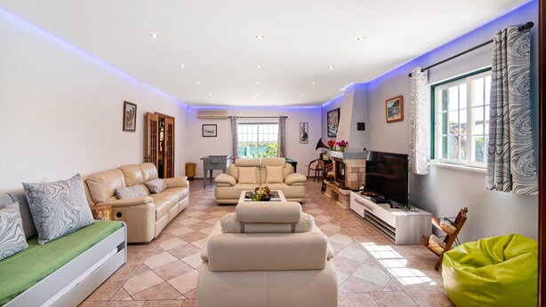 A spacious living room with a sofa set, a green bean bag, a flat-screen TV, and a fireplace.