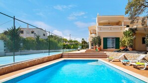 A swimming pool with a stone border, lounge chairs, and a building with a balcony.