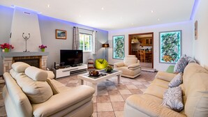 A living room with a sofa, armchair, coffee table, TV, fireplace, and artwork.