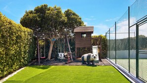 A fenced outdoor play area with a swing set, a small wooden structure, and a panda statue.