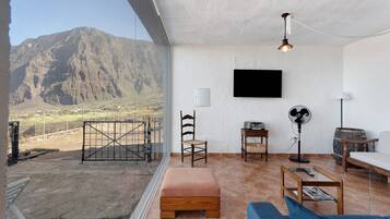 A living room with a mountain view, a television, a fan, and a wooden table.