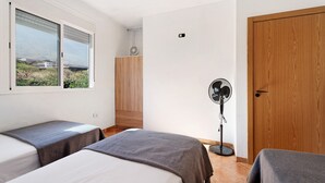 Un dormitorio con dos camas, un armario de madera, un ventilador de pie y una ventana con vistas.