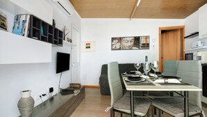 Ein moderner Essbereich mit einem Tisch für vier Personen, einem an der Wand befestigten Fernseher und einem durchgehenden Türrahmen einsehbarer Küchenbereich.