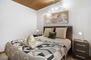 Quarto com cama, almofadas, mesa de cabeceira, abajur e um quadro na parede.
