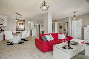 A modern living room with a red sofa, white chairs, a dining table, and a kitchen area in the background. - Holiday Apartment 'Vv Tamara Sunset Suite' with Sea Views, Private Terrace and Wi-Fi (Tacoronte)