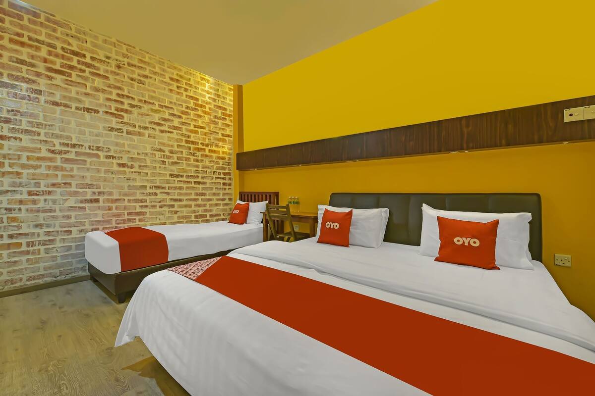 A hotel room with two beds, a brick wall, and a yellow accent wall.