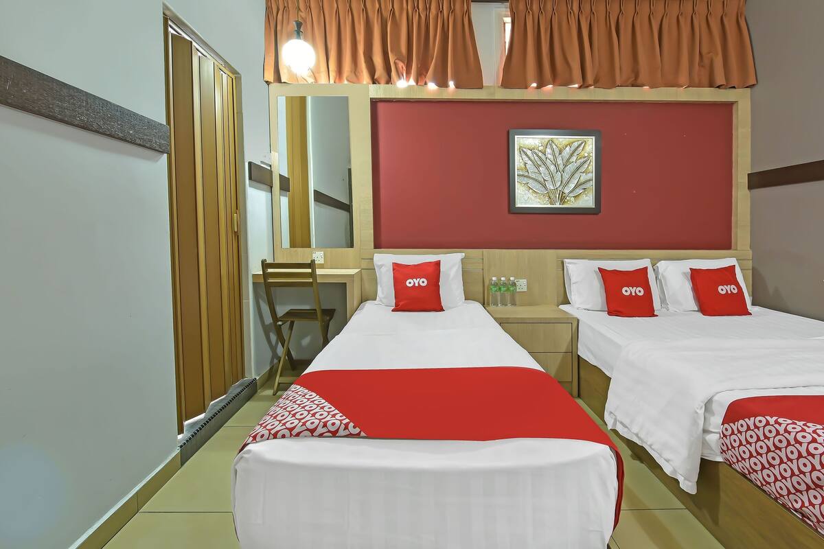 A hotel room with two beds, each with red and white bedding, a red wall, a framed artwork, and a wooden floor.