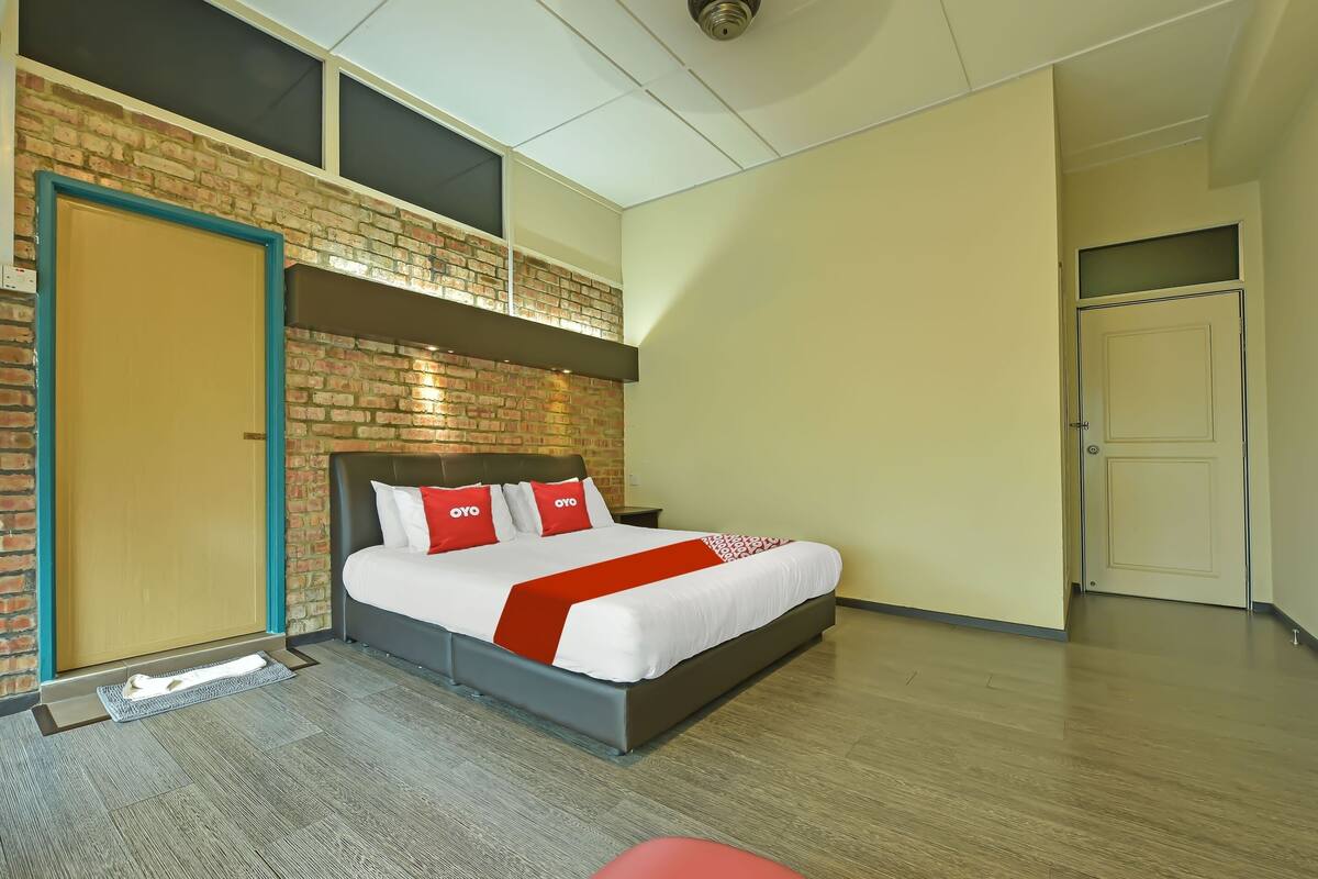 A modern hotel room with a brick accent wall, a large bed with red and white bedding, and a wooden floor.