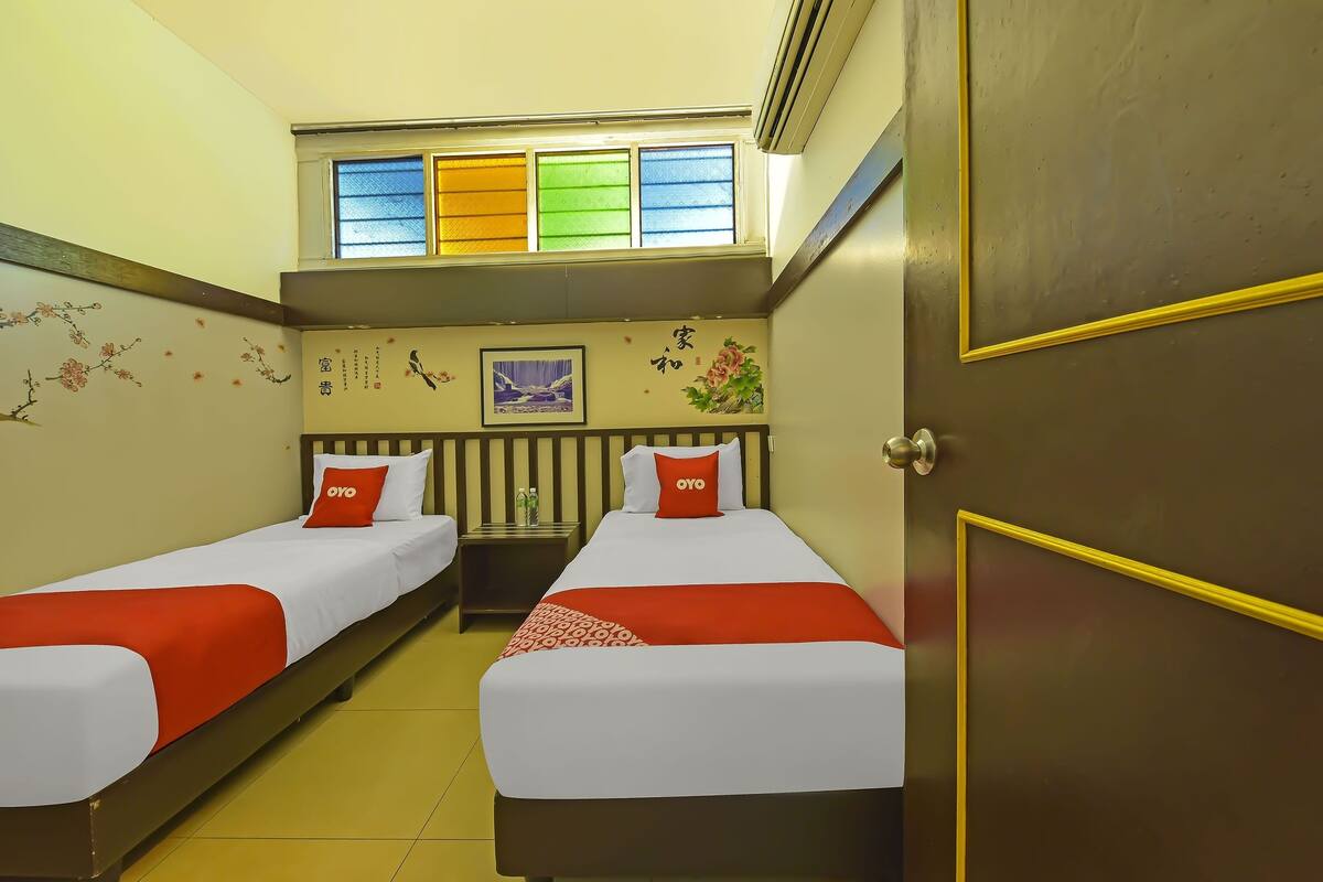 A hotel room with two beds, a window with colored blinds, a framed picture on the wall, and a door with a golden frame.