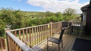 A wooden deck with a view of green hills and trees, a table with chairs, and a safety sign. - 12 Manleigh Park (Ilfracombe)