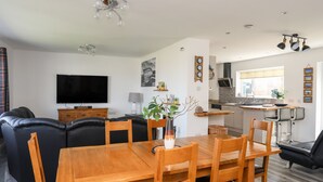 A modern living room with a wooden dining table, leather sofa, and a TV. - Tinkers Patch (Tyn-y-Gongl)
