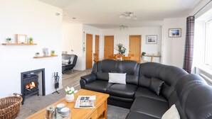 A modern living room with a black leather sofa, a fireplace, wooden shelves, and a dining area with a table and chairs. - Tinkers Patch (Tyn-y-Gongl)