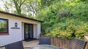 Een terras met rieten meubels en een glazen tafel, een deur met het opschrift 'Larchwood' en een houten omheining.