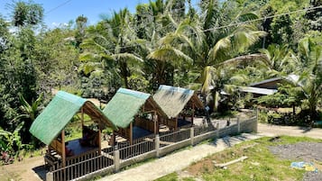 A row of thatched-roof huts with a concrete pathway in between, surrounded by lush greenery and palm trees.