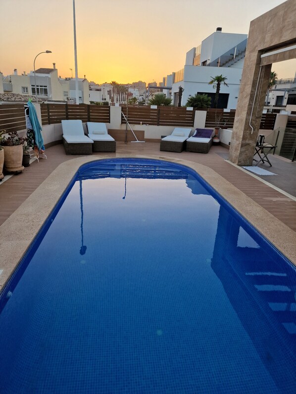 Ein Dachpool mit Liegestühlen und Blick auf die Skyline bei Sonnenuntergang.