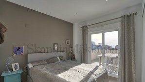 Ein Schlafzimmer mit einem großen Bett, einem Nachttisch, einem Fenster mit Vorhängen und Blick auf Gebäude.