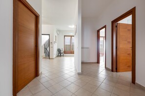Un pasillo amplio con puertas de madera y suelo de baldosas, que conduce a una escalera y una zona de estar.