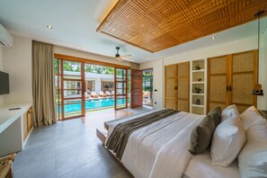 Ein Schlafzimmer mit einem großen Bett, einem Fernseher, einem Deckenventilator und Blick auf einen Swimmingpool.