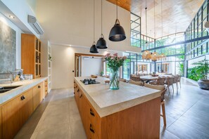A spacious kitchen with a large island, wooden cabinets, and pendant lighting. - Villa KClub River Front 4 (Canggu)