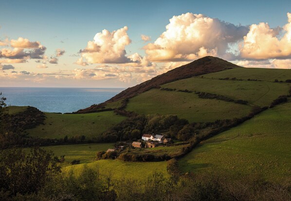 A rural landscape with rolling hills, a body of water, and a small cluster of houses.