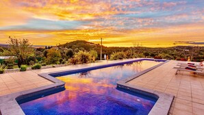 Piscina com vista para o pôr do sol sobre uma paisagem montanhosa.