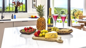 Uma bancada de cozinha com abacaxi, garrafa de champanhe, copos de martini e tábua de queijos com morangos e uvas.
