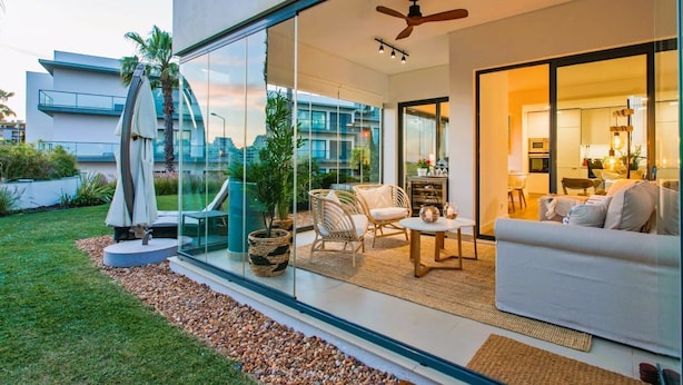 Une maison moderne dotée d’un patio entièrement vitré, de mobilier d’extérieur et offrant une vue sur le paysage urbain.