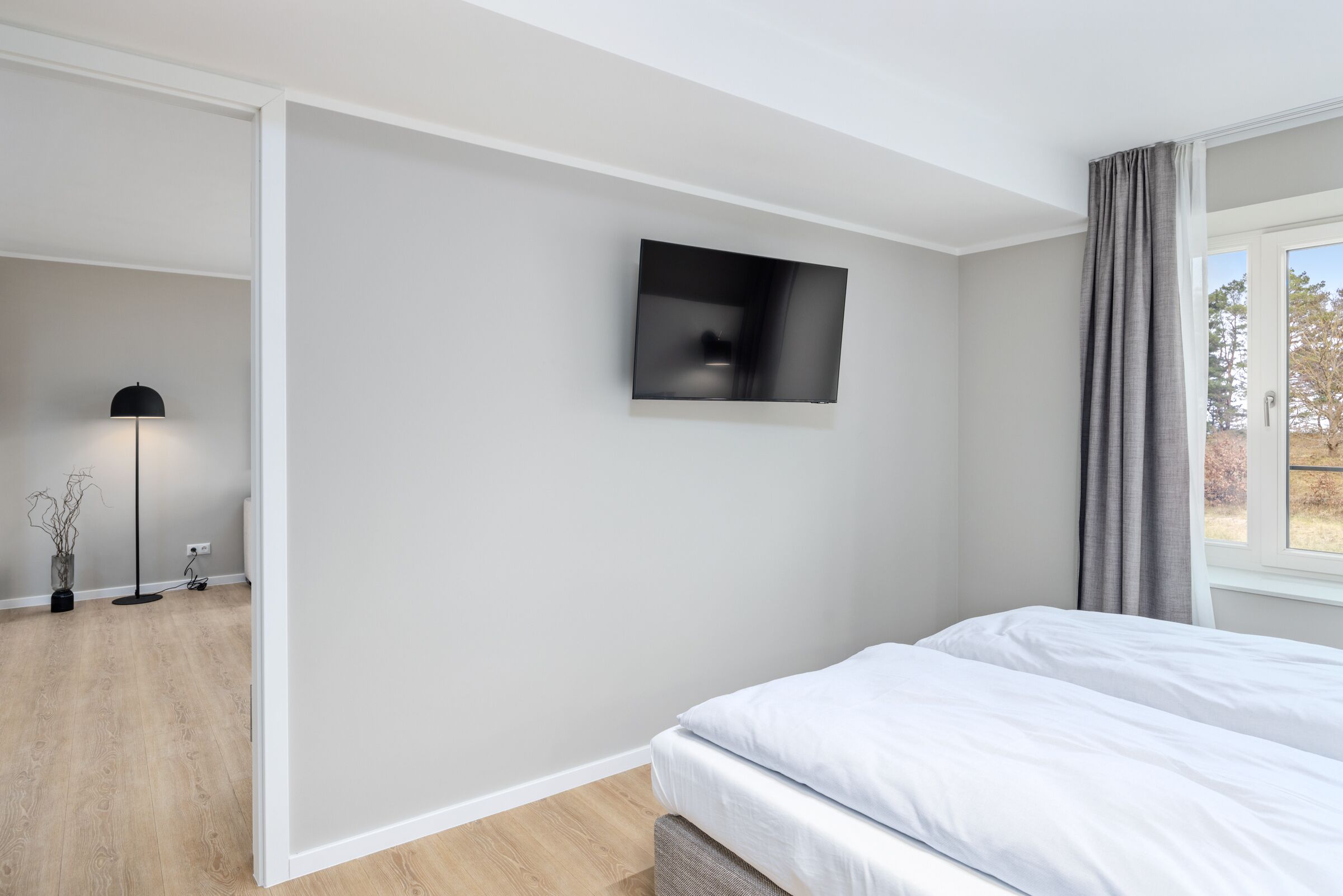 Un dormitorio moderno con una cama, un televisor de pantalla plana montado en la pared y una ventana con cortinas.