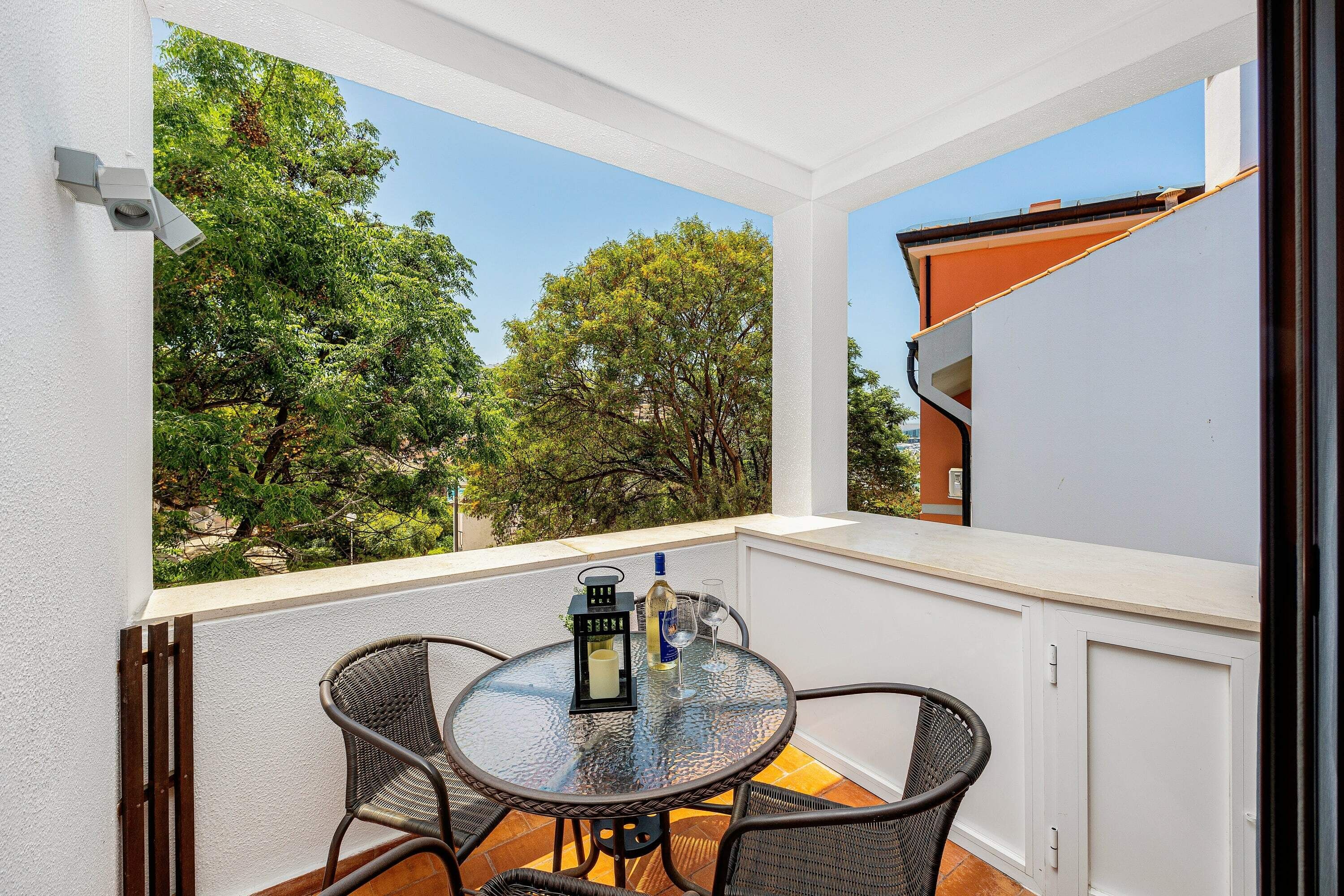 A balcony with a glass table, wicker chairs, and a bottle of wine.