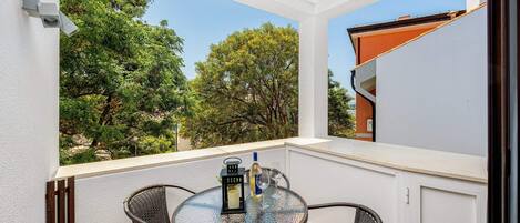 A balcony with a glass table, wicker chairs, and a bottle of wine.