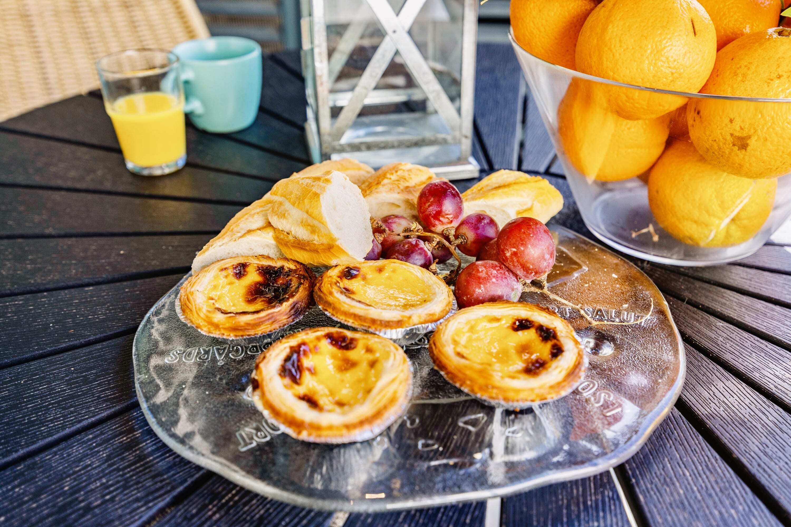 A breakfast setting with pastries, grapes, and oranges on a table.