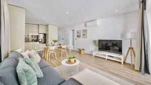 Ein modernes Wohnzimmer mit einem grauen Sofa, einem runden Couchtisch, einem Fernseher und einem Essbereich im Hintergrund.