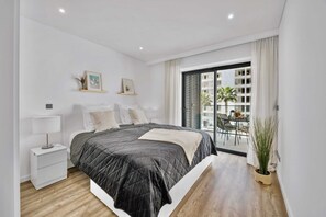 Un dormitorio moderno con una cama grande, mesitas de noche, una ventana con persianas y vistas al balcón exterior.