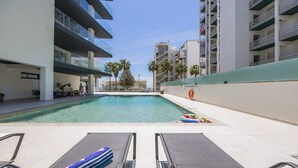 A modern hotel pool area with clear blue water, lounge chairs, and a lifebuoy. - Stylish Modern Beachside Apartment with Pool & Seaview (Quarteira)