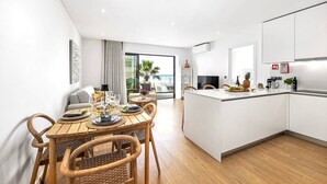 A modern kitchen with a central island, a dining area with a wooden table and chairs, and a view of the ocean through large windows. - Stylish Modern Beachside Apartment with Pool & Seaview (Quarteira)
