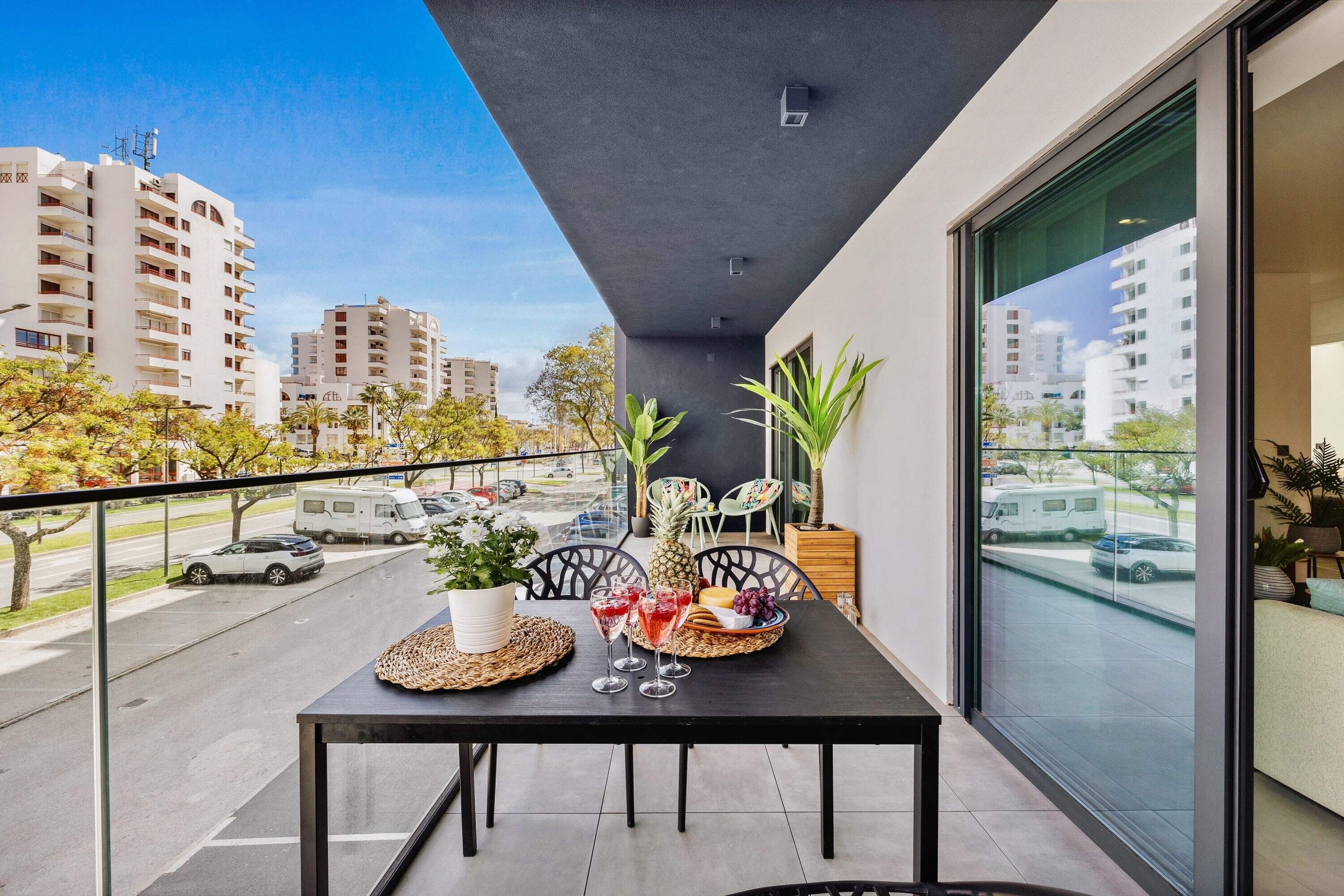 A balcony with a table set for two, featuring a woven placemat, two wine glasses, and a fruit basket.